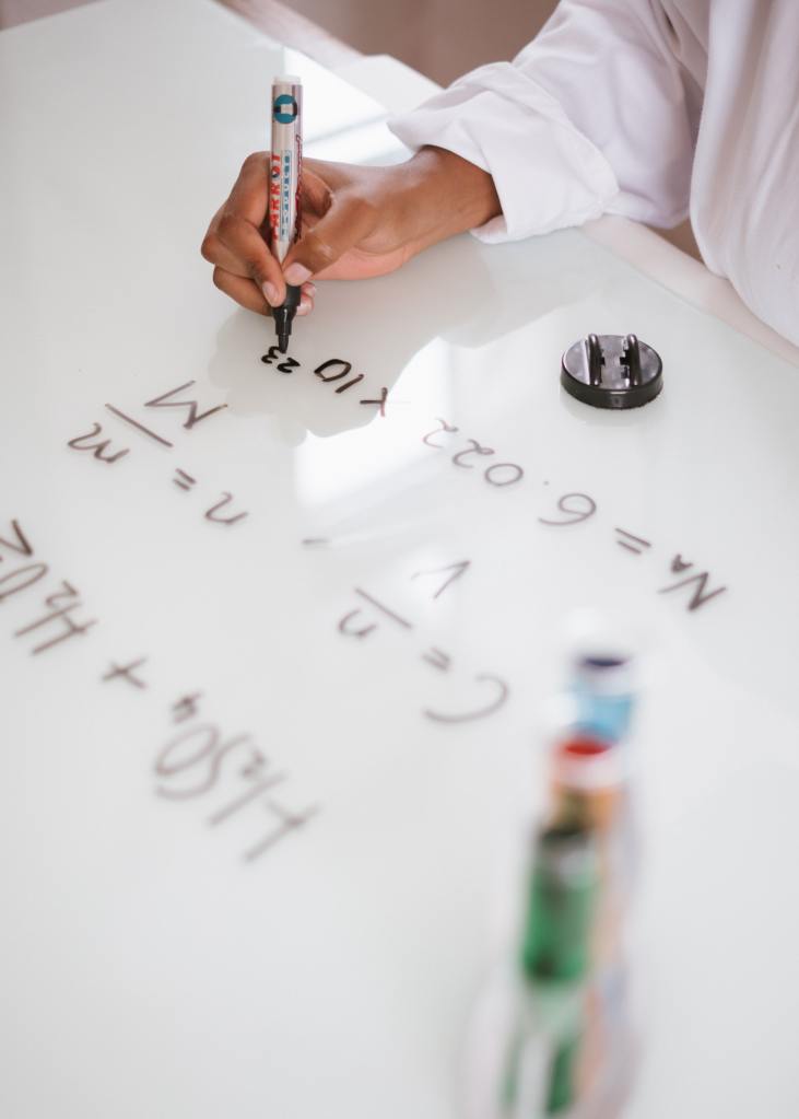 Person writing equations on whiteboard with a black dry-erase marker